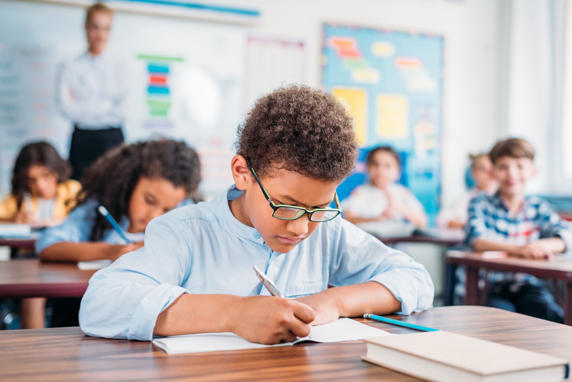 african american schoolboy writing in notebook at school